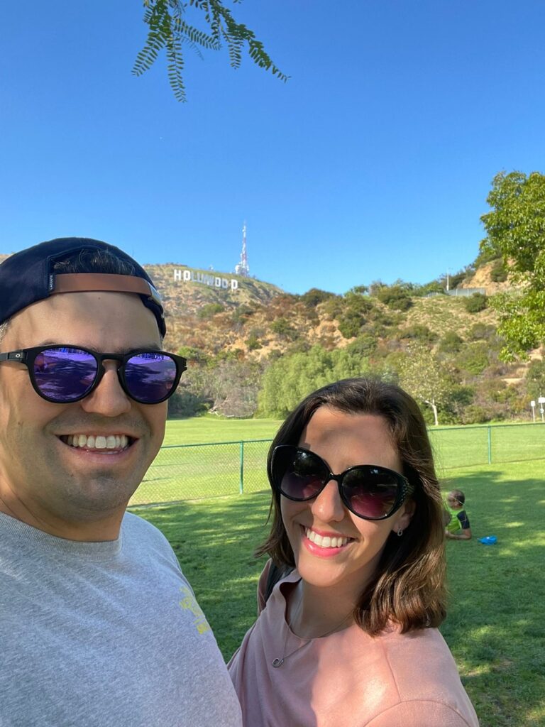 selfie de homem com mulher em gramado com montanha e letreiro ao fundo