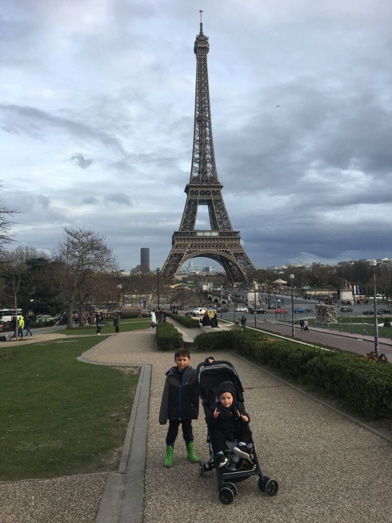 menino e bebê em carrinho em frente a Torre Eiffel.