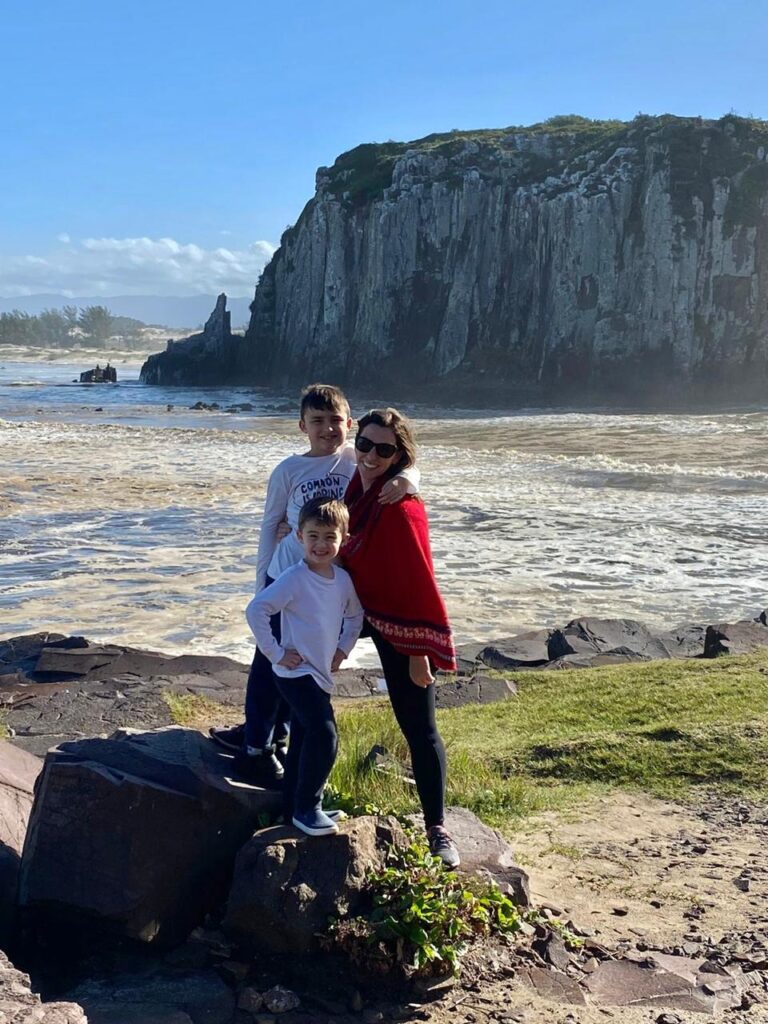 mulher e dois meninos com praia e penhasco ao fundo,