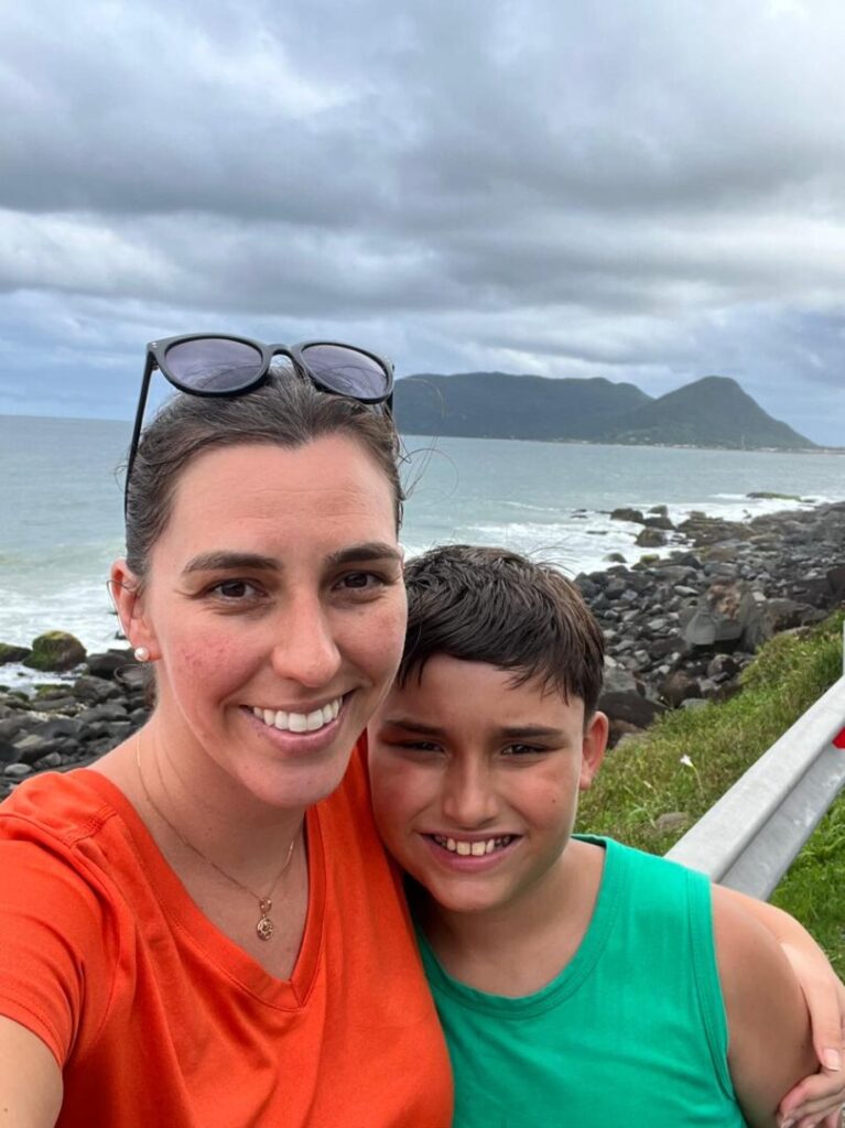 mãe e filho com vista de praia de pedras ao fundo.