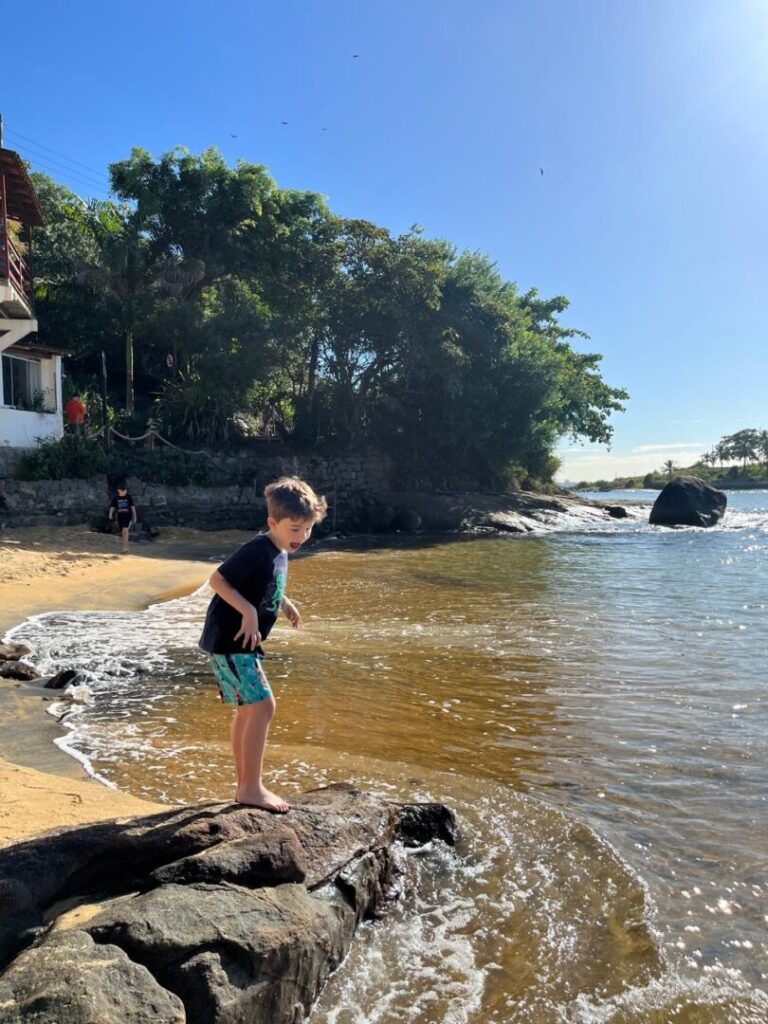 Menino em cima de pedra na praia.