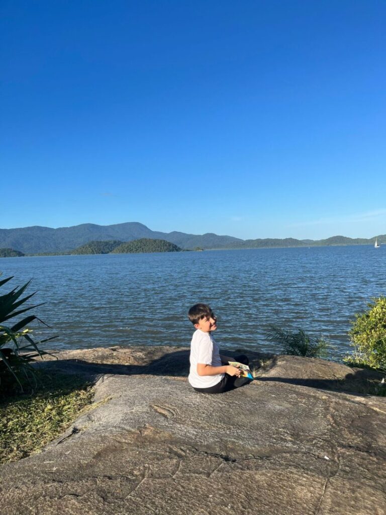 menino sentado em pedra com mar ao fundo.
