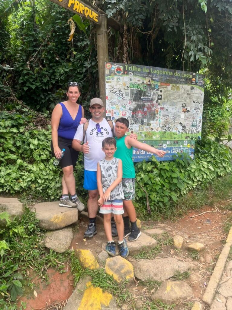 familia de pai , mãe e dois meninos ao lado de placa de início de trilha