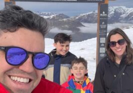 familia de pai, mãe e dois meninos em letreiro com montanha de neve ao fundo