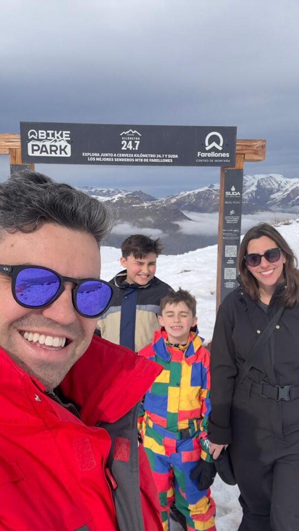 familia de pai, mãe e dois meninos em letreiro com montanha de neve ao fundo